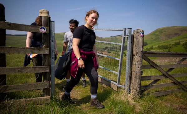 A young woman with blonde hair smiling at the camera as she walks through a rural gate