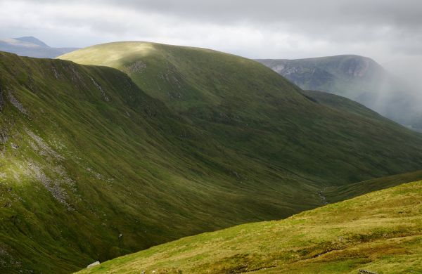 A steep, green valley drops away to the centre, as rain rolls in from. 