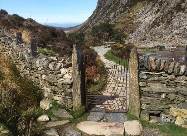 A metal gate designed to look like contours on a map, set within a dry stone wall with distant countryside views beyond