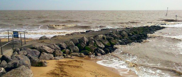 A rocky pier jets out from a sandy beach into the breaking waves of the sea