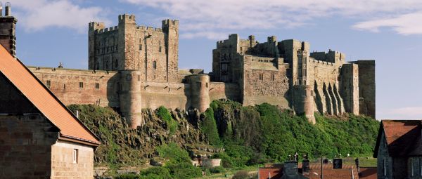 The imposing Bamburgh Castle sits on top of a large rocky mound, looking out over the roofs of the town's more modern houses