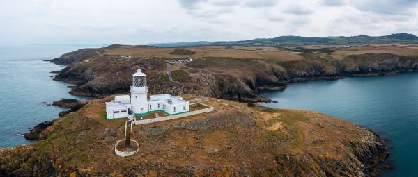 A small white lighthouse sits on a round, rocky island just off the mainland