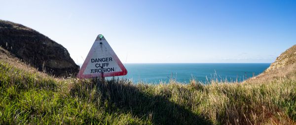 "Danger cliff erosion" sign on a sandy cliff edge