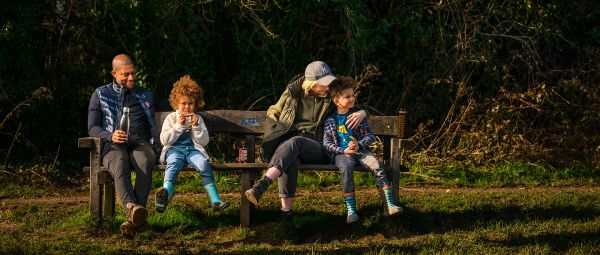 A family of four sitting on a bench outdoors having a drink