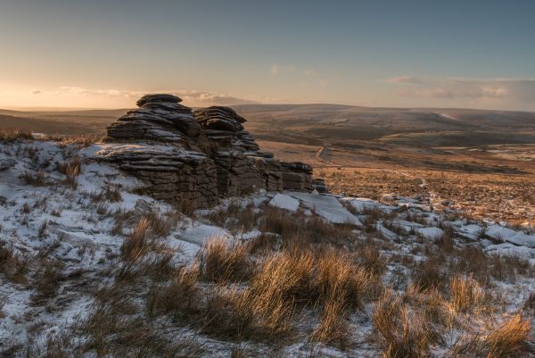 A granite outcrop sits on snowy ground, overlooking the expanse of Dartmoor