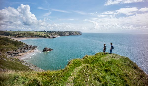 Two young children stand on top of a cliff overlooking a pair of sandy bays