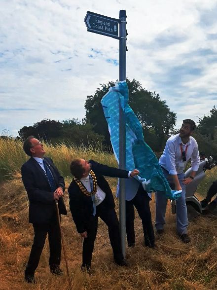 People removing a cloth from the new England Coast Path sign