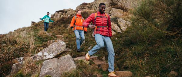 Three young walkers make their way down some stone steps, embedded into the hillside, in the Northumberland hills