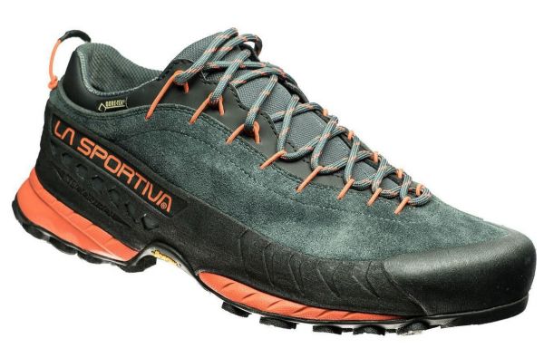 A cloe up of a single walking shoe with a deep green suede leather upper and orange detailing on the laces and sole