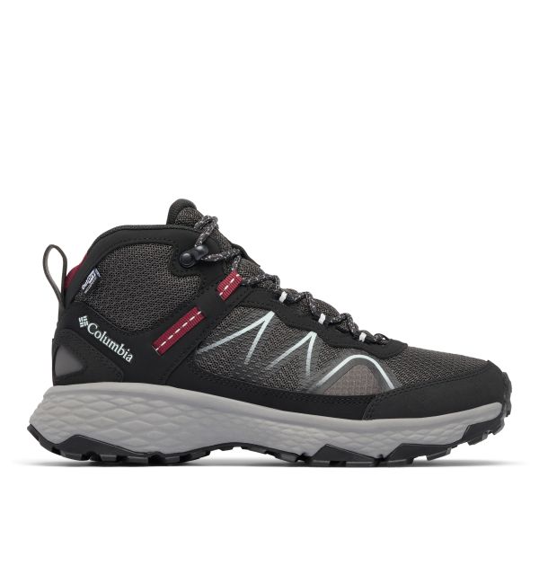A single Columbia mid‑cut hiking shoe in black and grey with red accents. It features a breathable mesh upper, synthetic overlays, white zigzag side stitching, a rugged traction outsole, padded collar and tongue, and a heel pull tab. The Columbia logo and an “OutDry” waterproof tag are visible.