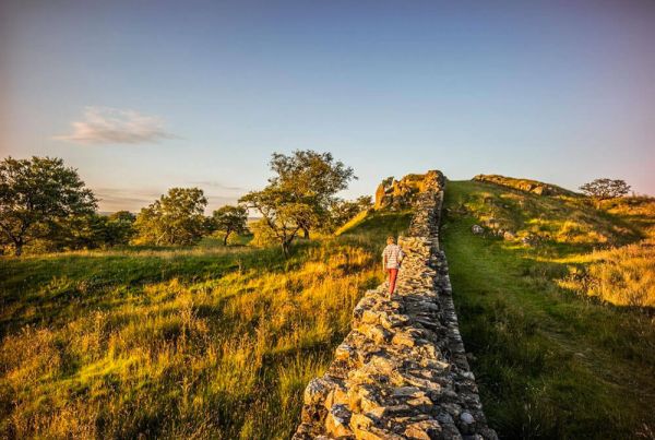 A person walking along a long stone wall