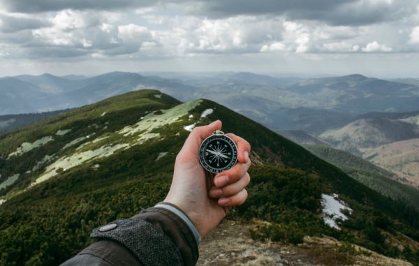 A hand holding a compass at the top of a mountain