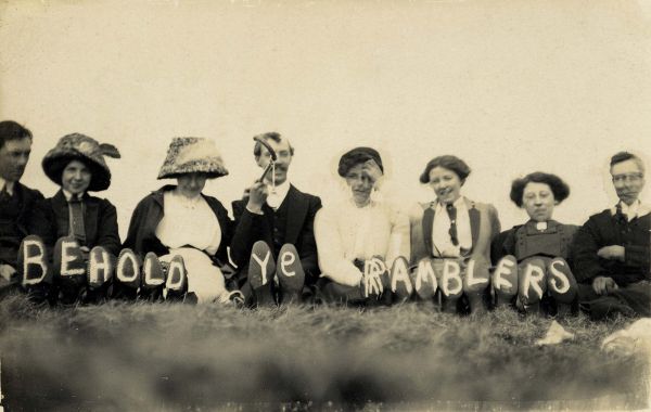 Black and white photo of people seated upon a hill, with Behold Ye Ramblers printed on the sole of their shoes