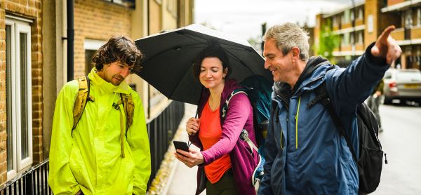 Two men and a woman on an urban street, looking at a phone and pointing in the direction of travel