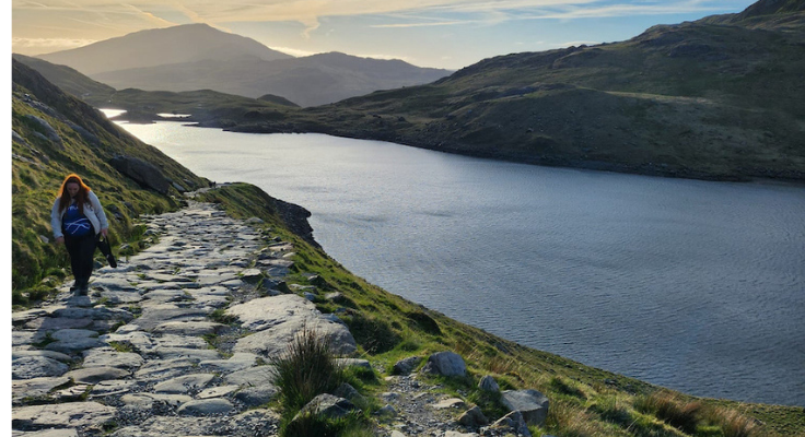 A cobbled path climbs a hillside next to an azure lake